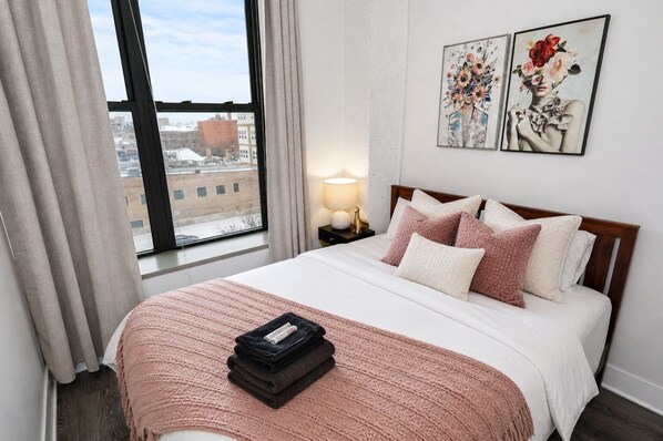 A hotel room with a large bed, a nightstand with a lamp, and two paintings on the wall. - McCormick Place 2b/2b corner unit with optional parking for up to 6 guests (Chicago)