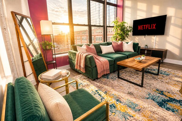 A modern living room with a green sofa, a wooden coffee table, and a TV mounted on the wall.