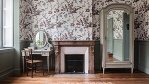 A room with floral wallpaper, a mirror, a fireplace, and a wooden floor. - Deluxe double room (Le Pian-Médoc)