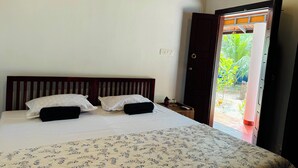A bedroom with a bed, pillows, a nightstand, and a door leading to a balcony. - Beach Front Home in Marari : Marari Helen Villa (Mararikulam)