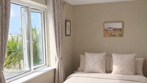 A bedroom with a large bed, a window with curtains, a ceiling light, and a framed picture on the wall.