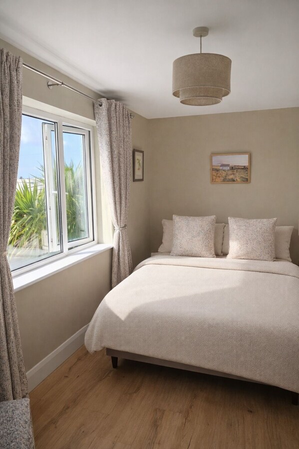 A bedroom with a large bed, a window with curtains, a ceiling light, and a framed picture on the wall.