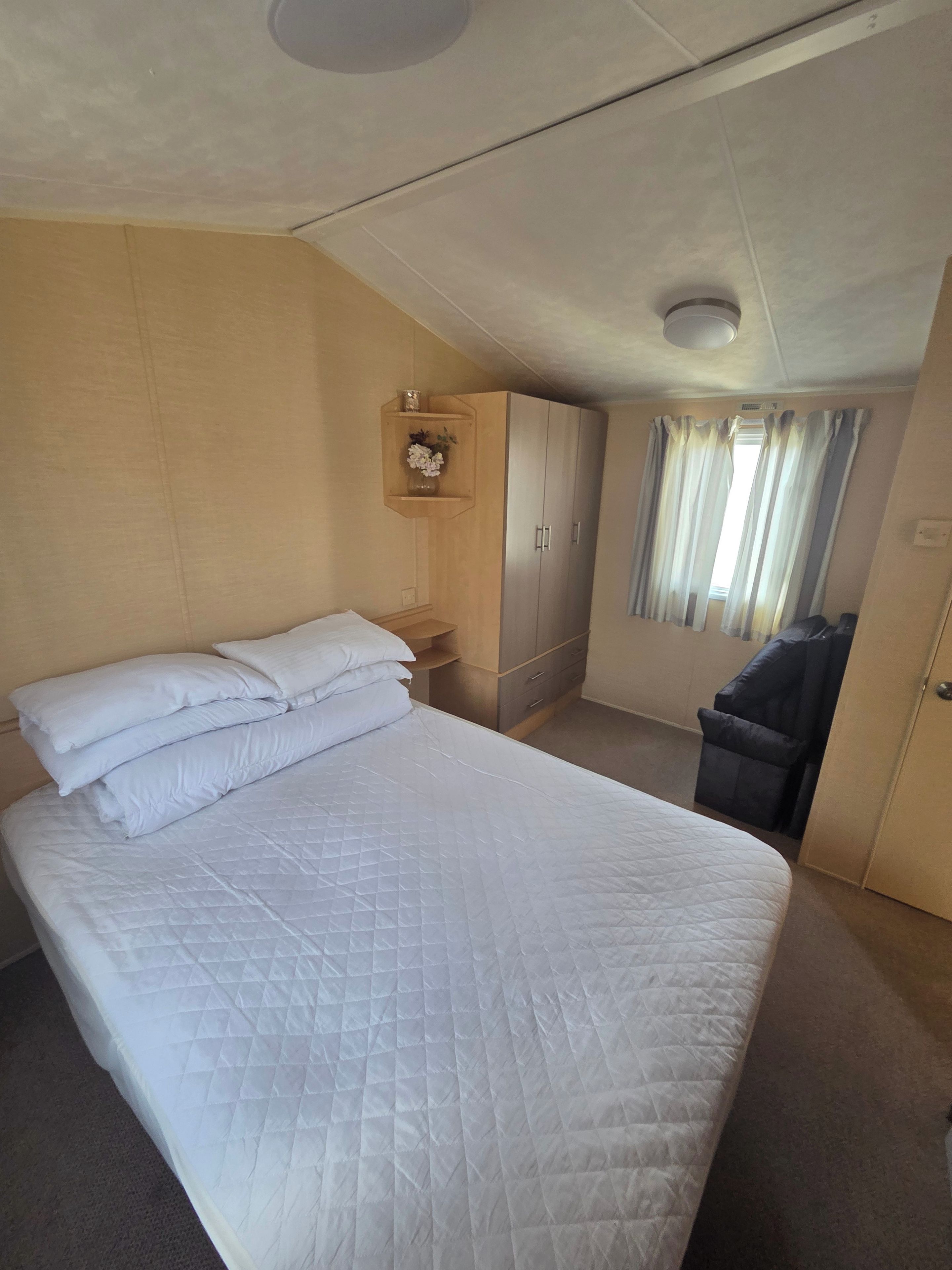 A hotel room with a large bed, a wardrobe, a small table with a vase, and a window with curtains.