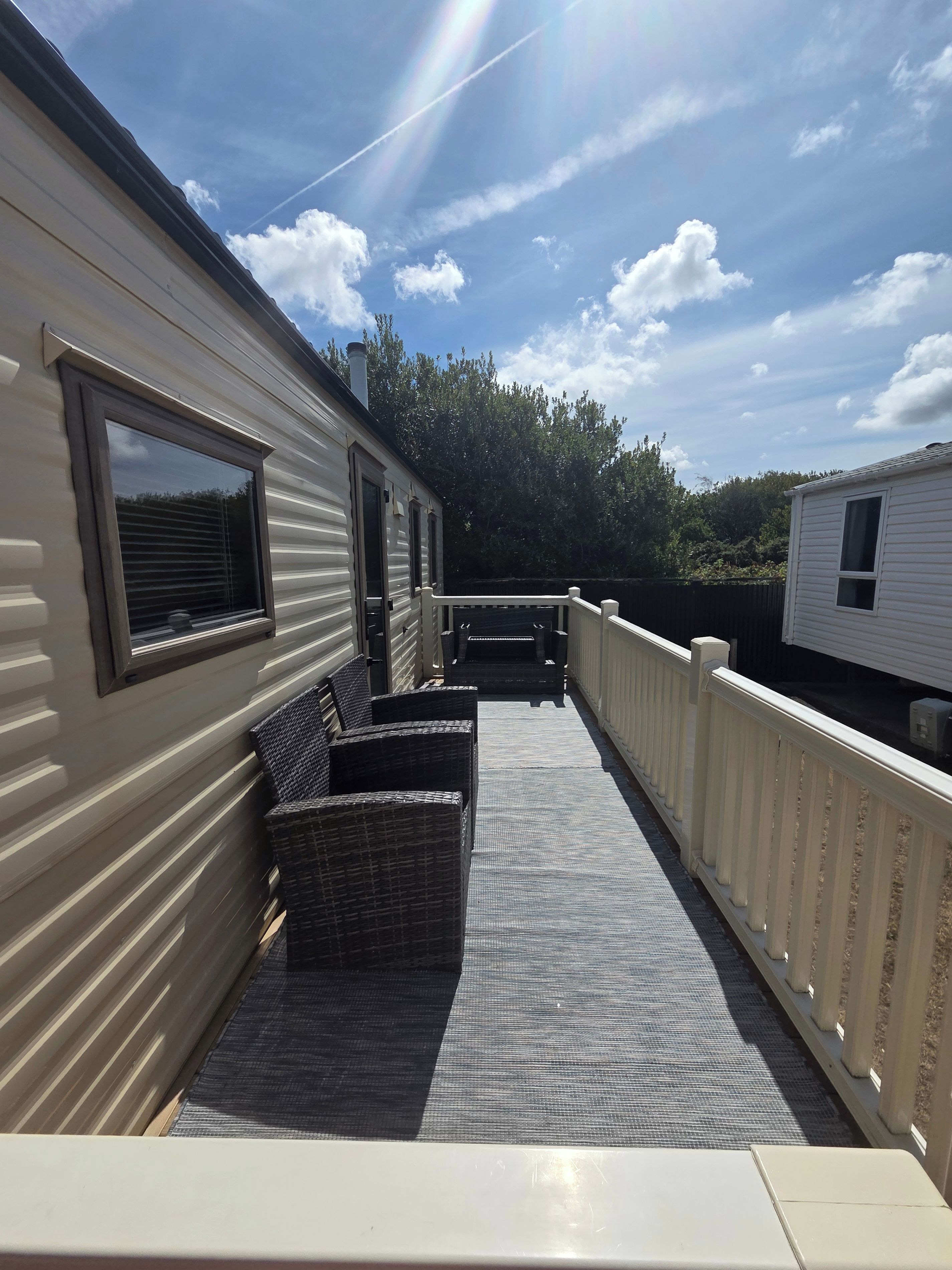 A covered outdoor deck with seating, a railing, and a view of the sky and trees.