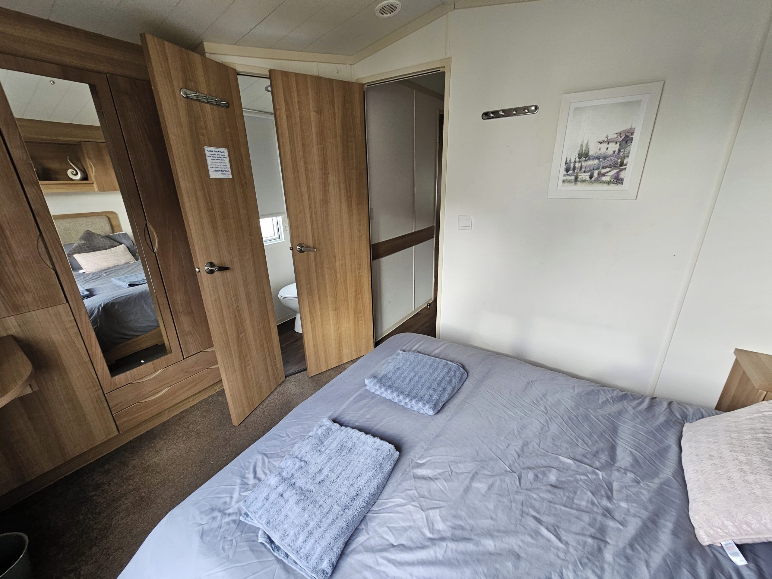 Ein Schlafzimmer mit einem Bett, einem Holzschrank, einem Spiegel und einem Bild an der Wand.