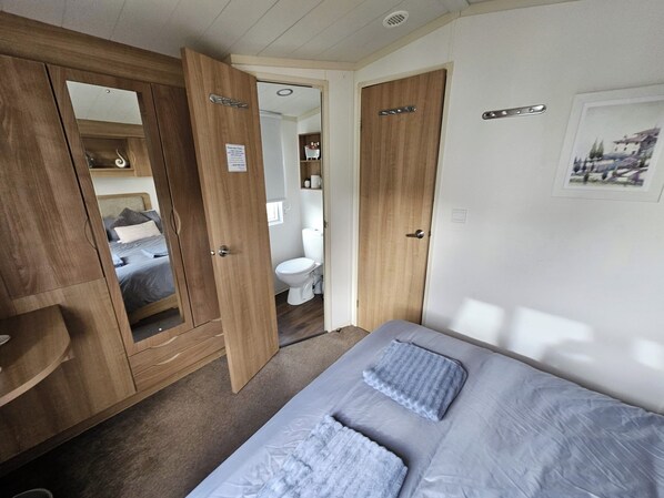 A bedroom with a bed, wooden wardrobe, and a bathroom with a toilet and sink. - Heidi Cabin Sleeps 6 With Free Parking (Rhyl)