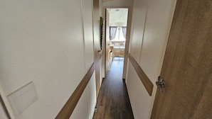 A narrow hallway with wooden flooring and white walls, leading to a room with a bed and curtains. - Heidi 2 Bed Robin Hood (Rhyl)