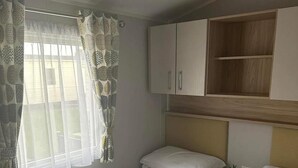 Una habitación con dos camas individuales, un cabecero de madera, una mesita de noche con una planta y una ventana con cortinas estampadas.