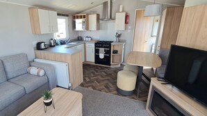 Ein kompaktes Wohnmobil-Interieur mit Küchenzeile, einer Sitzecke, einem Fernseher und einem kleinen Tisch mit Pflanze.