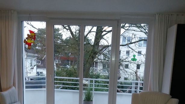 Un soggiorno moderno con due poltrone bianche, un poggiapiedi bianco e una grande porta scorrevole in vetro che dà su un balcone esterno.