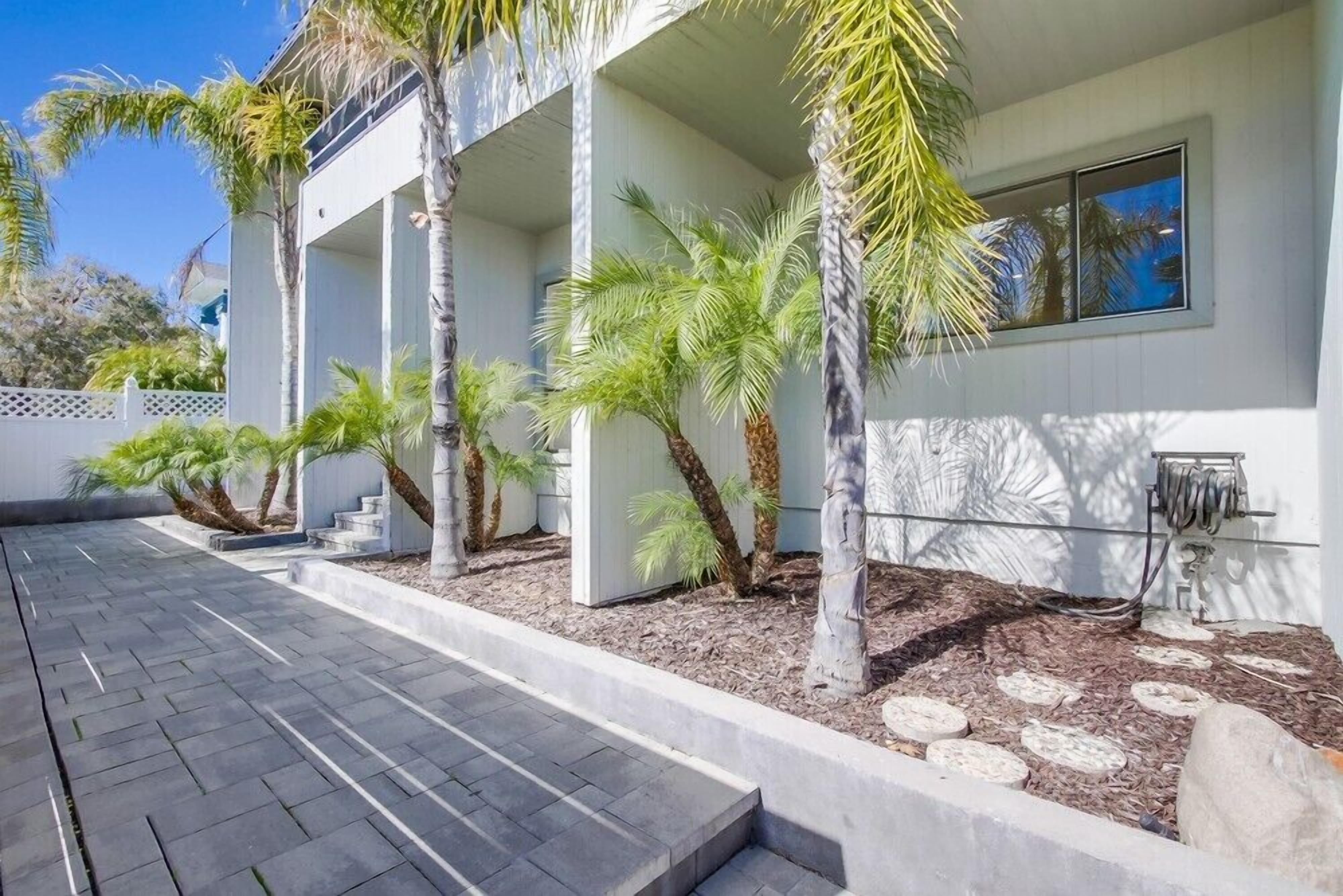 A modern building with a covered outdoor area, palm trees, and a paved walkway.