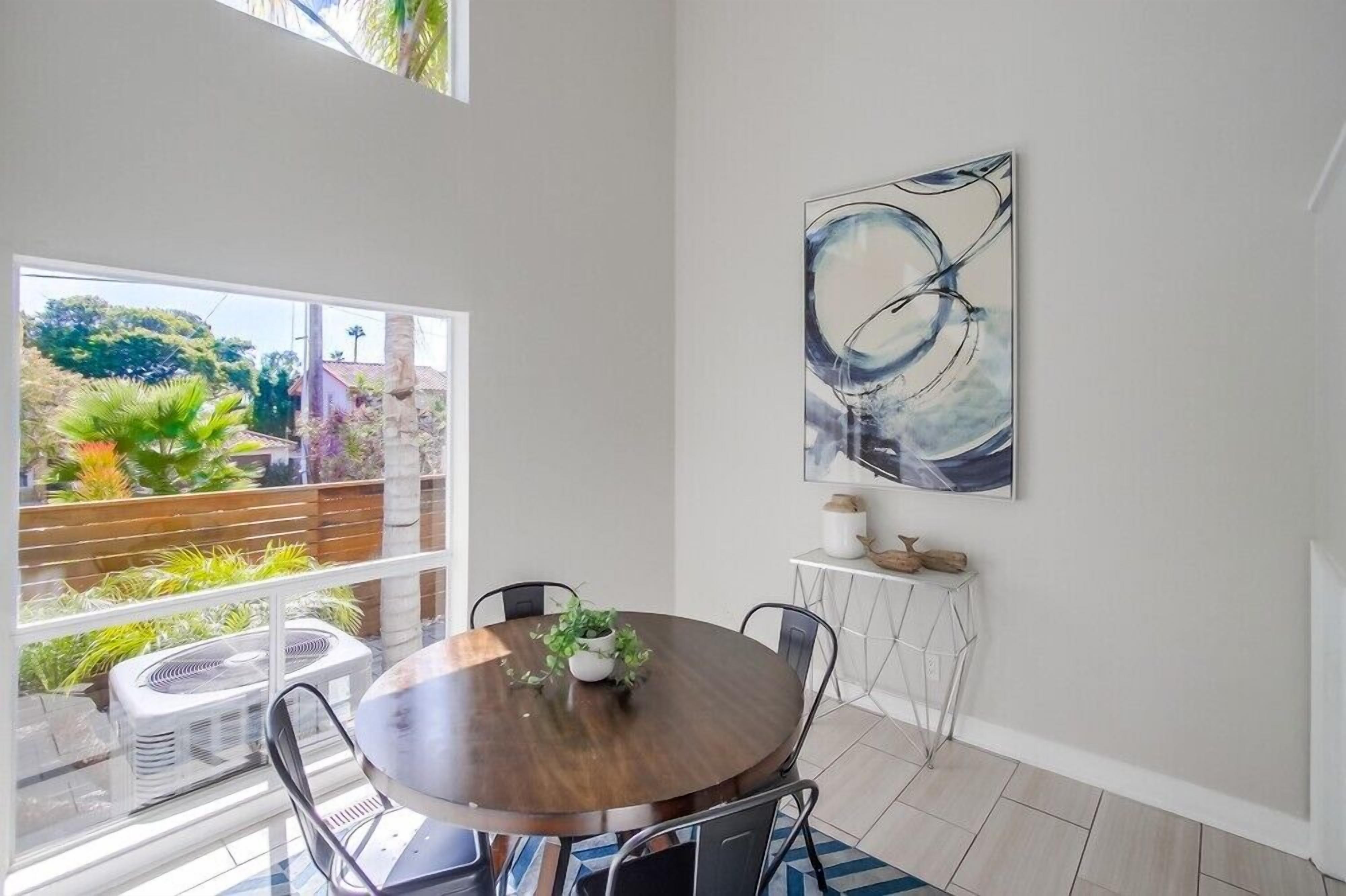 A dining area with a round table, chairs, a potted plant, and a large abstract painting on the wall.