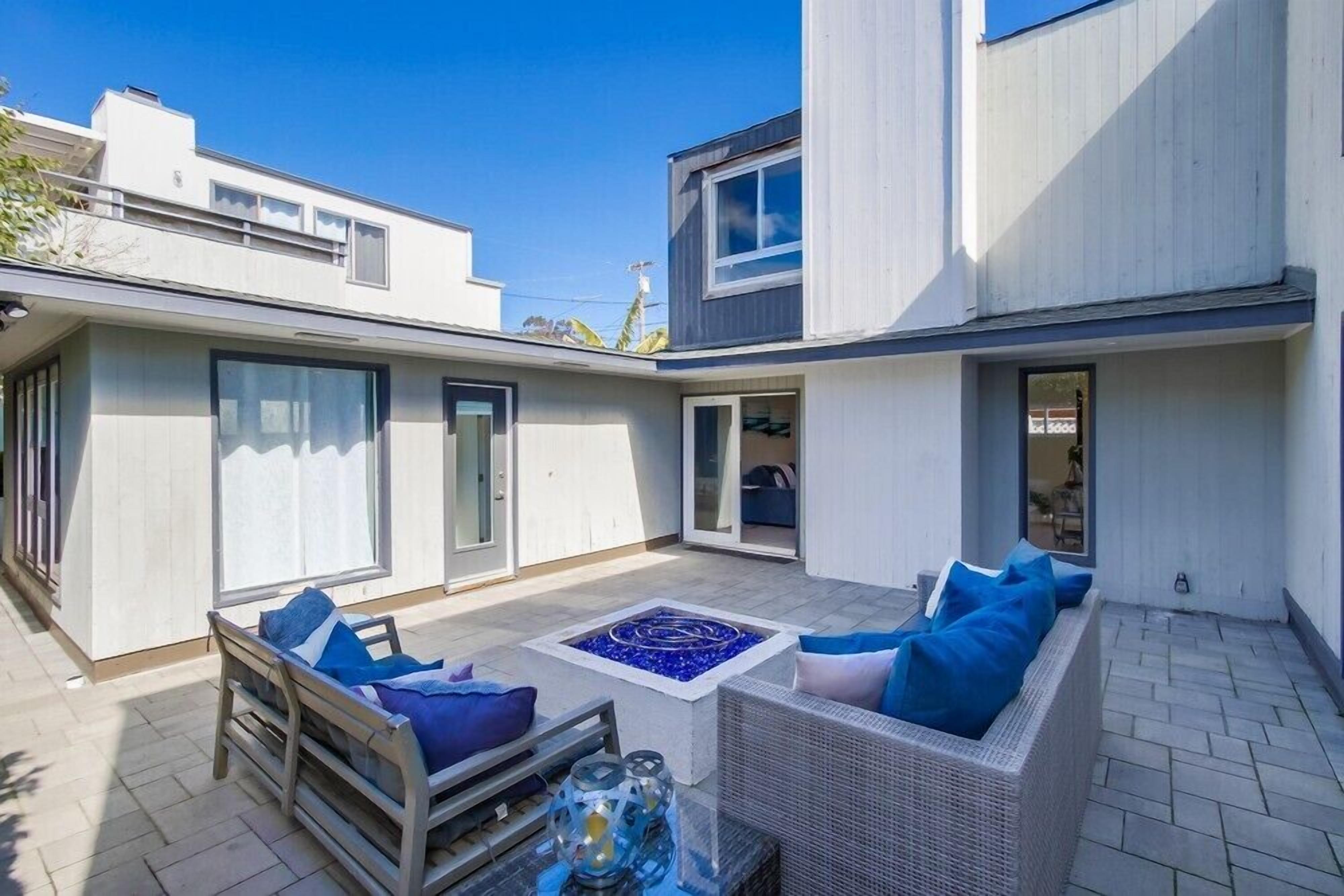 A modern outdoor patio with a wicker sofa, a small table, and a fire feature.