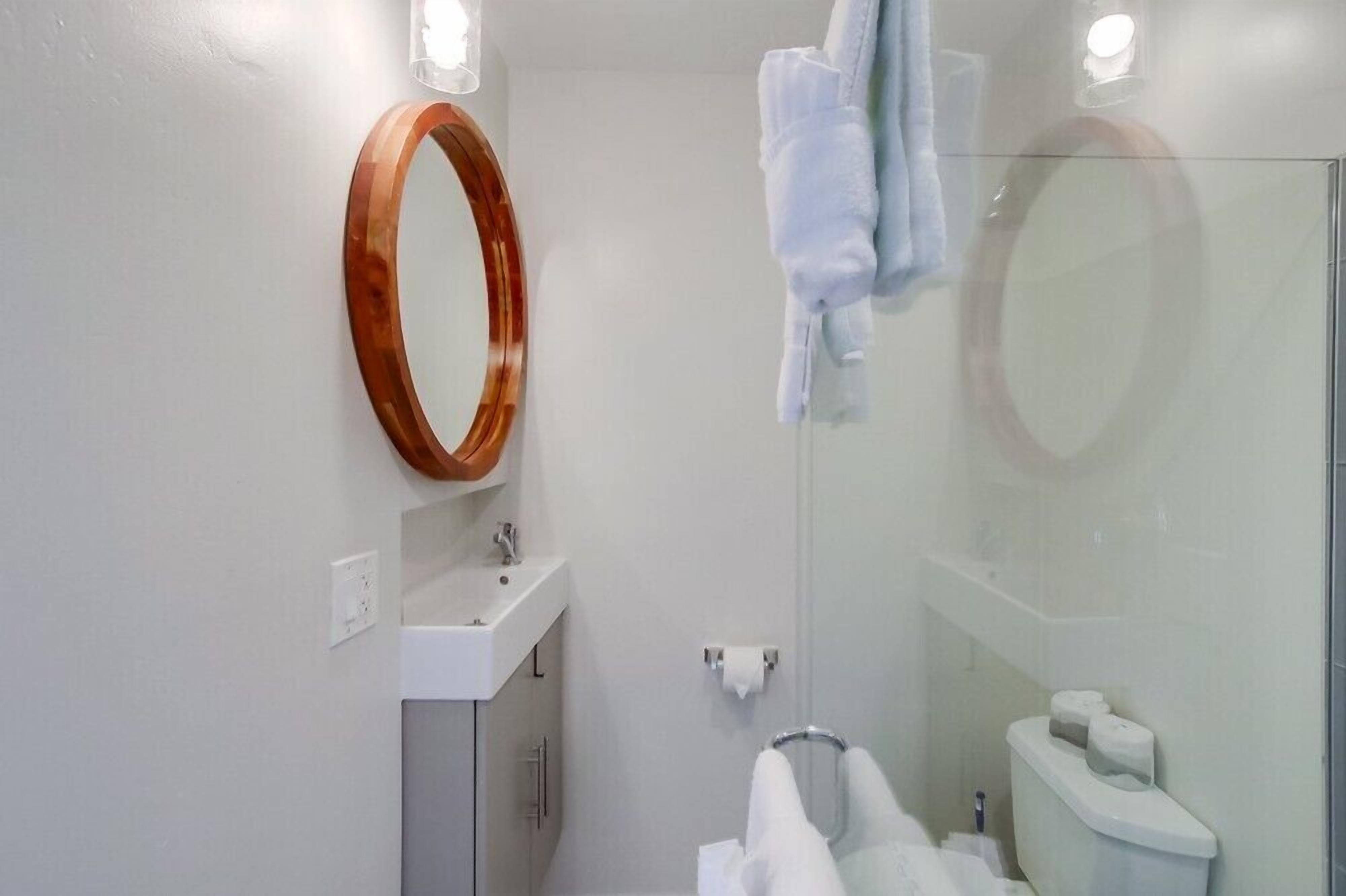 Une salle de bain moderne avec un miroir à cadre en bois, un lavabo blanc et une cabine de douche en verre.