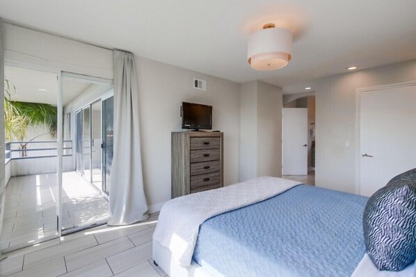 Une chambre à coucher comprenant un lit, une télévision, une commode et une porte-fenêtre coulissante donnant sur un balcon.