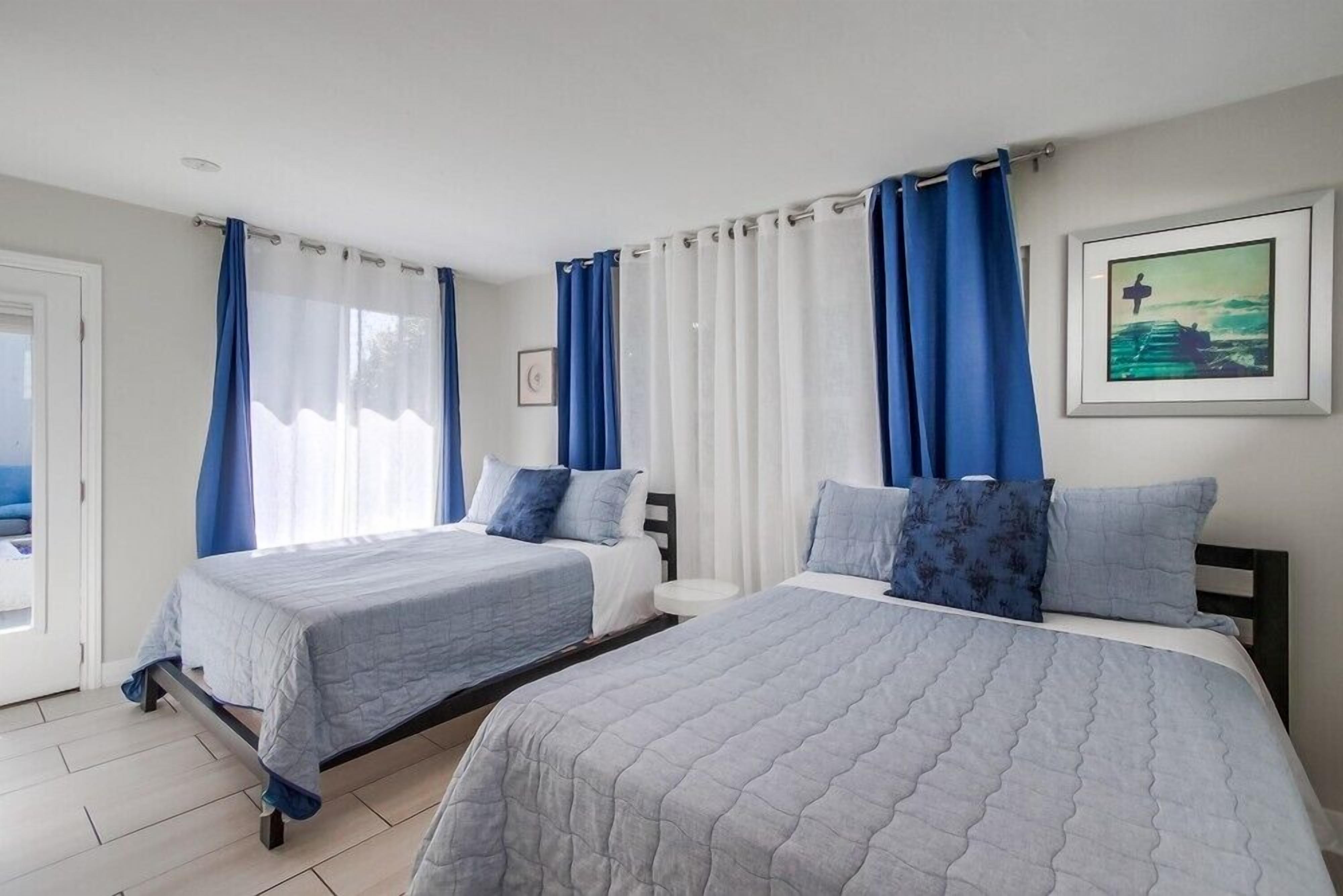 A hotel room with two beds, a small round table, and a painting on the wall.