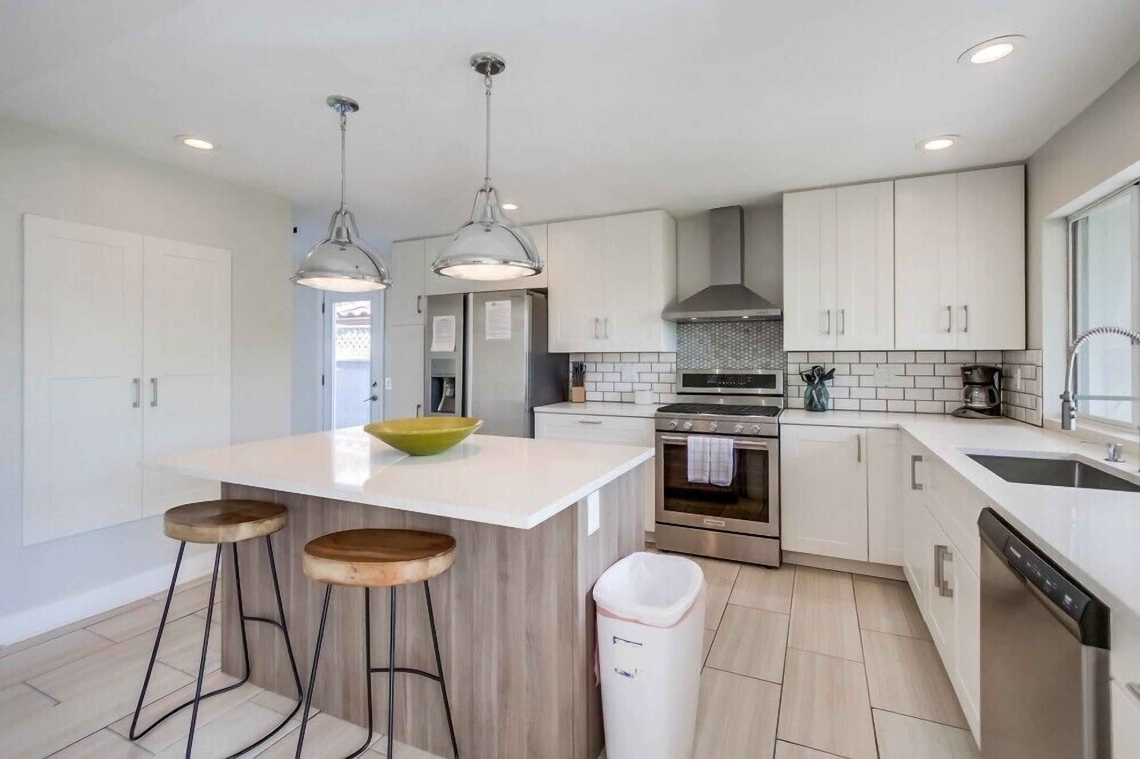 A modern kitchen with white cabinets, a central island with stools, stainless steel appliances, and pendant lighting.
