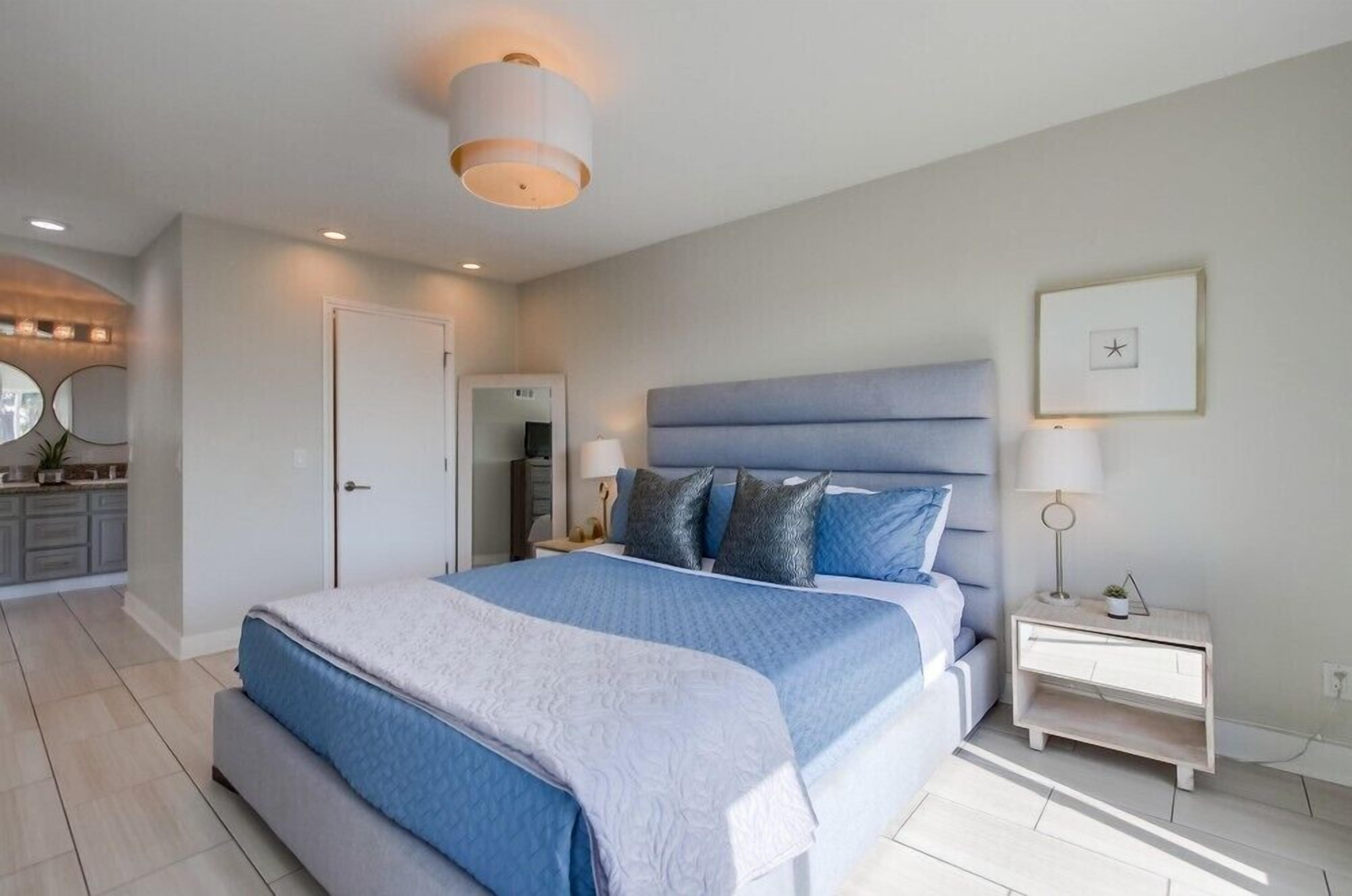 Een moderne slaapkamer met een groot bed, nachtkastjes, een spiegel en een deur.