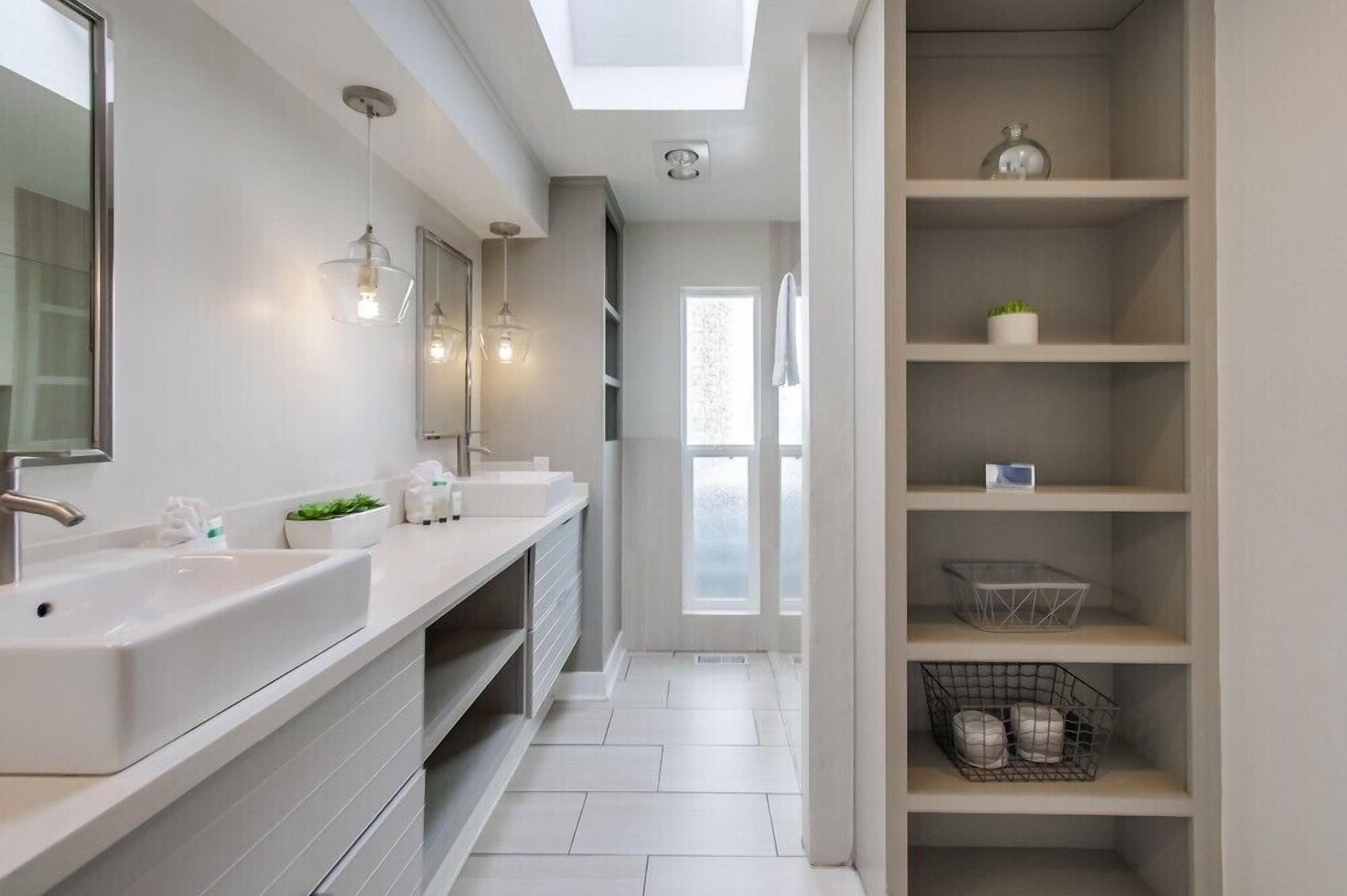 Een moderne badkamer met twee wastafels, een grote spiegel en ingebouwde planken.