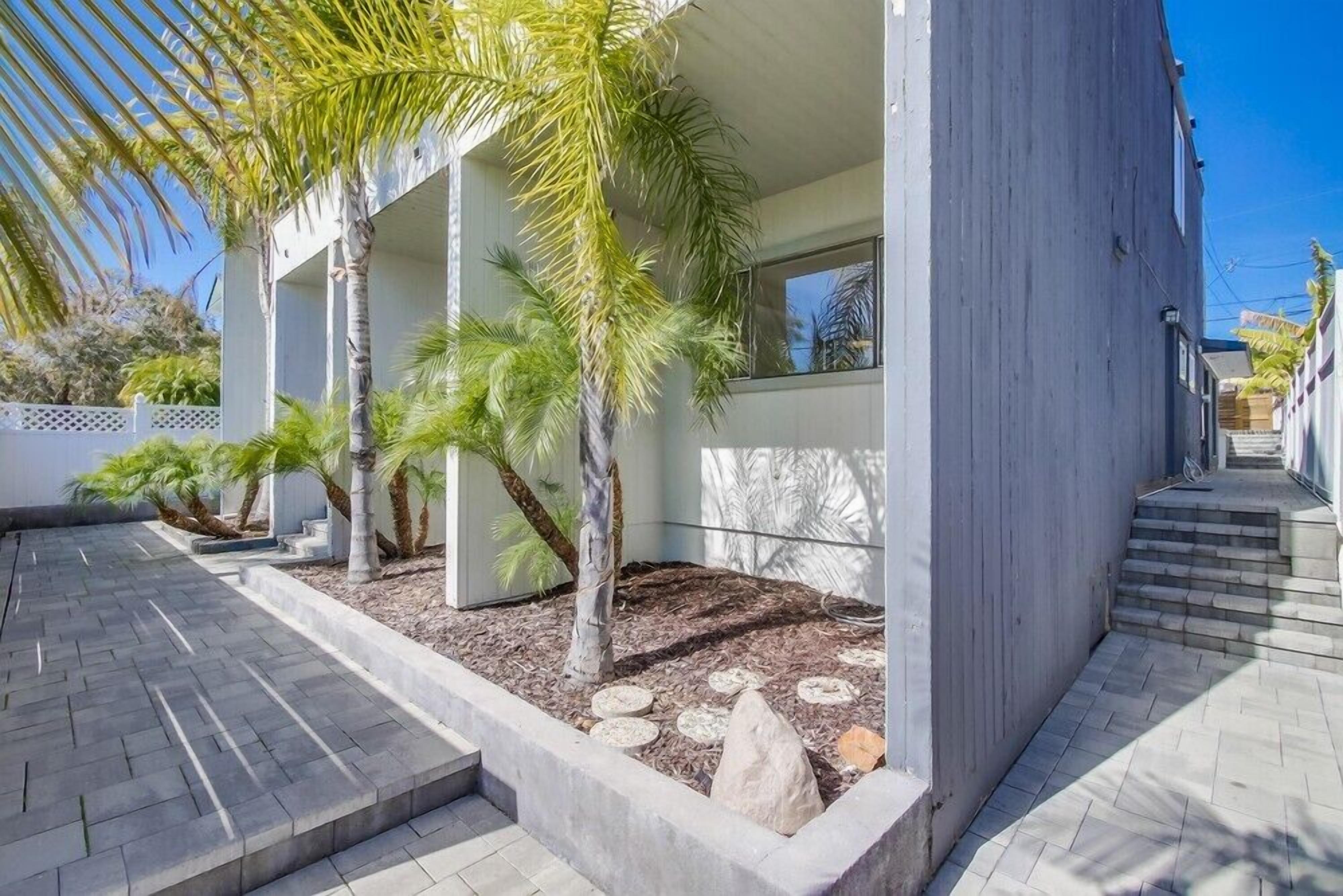 A modern building with a concrete facade, a paved walkway, and palm trees.