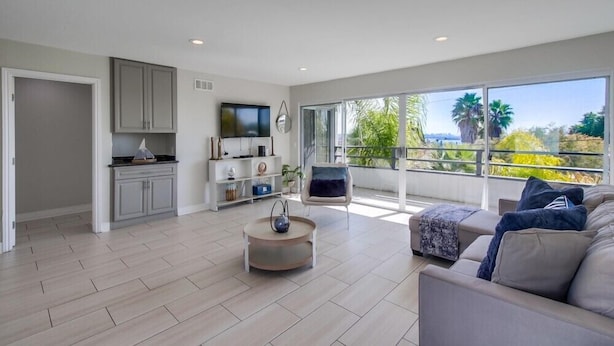 A spacious living area with a modern kitchen, large windows offering a view of greenery, and a comfortable seating area. - Beryl Retreat (San Diego)