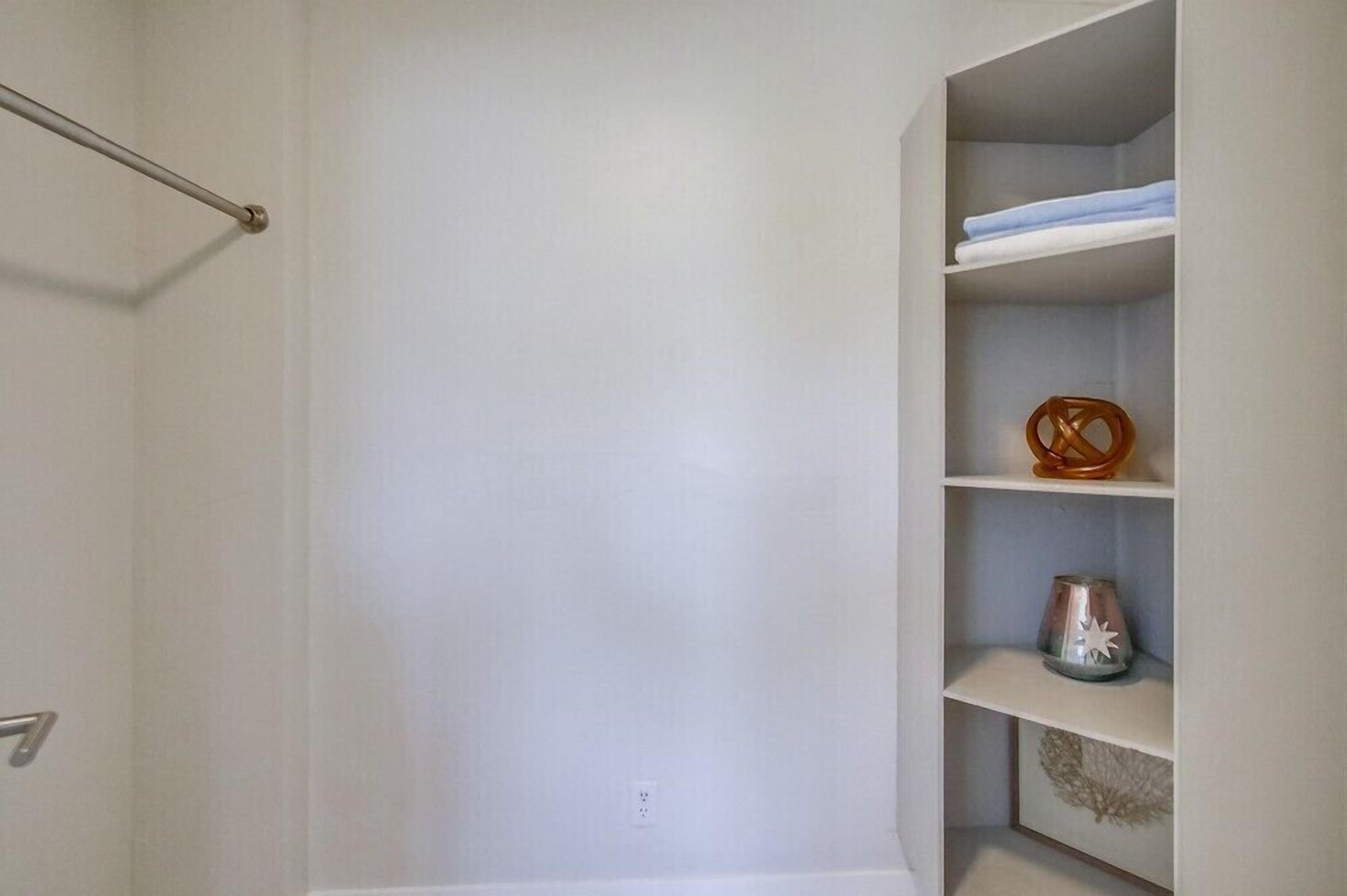 A white closet with shelves containing folded clothes, a decorative item, and a framed picture.