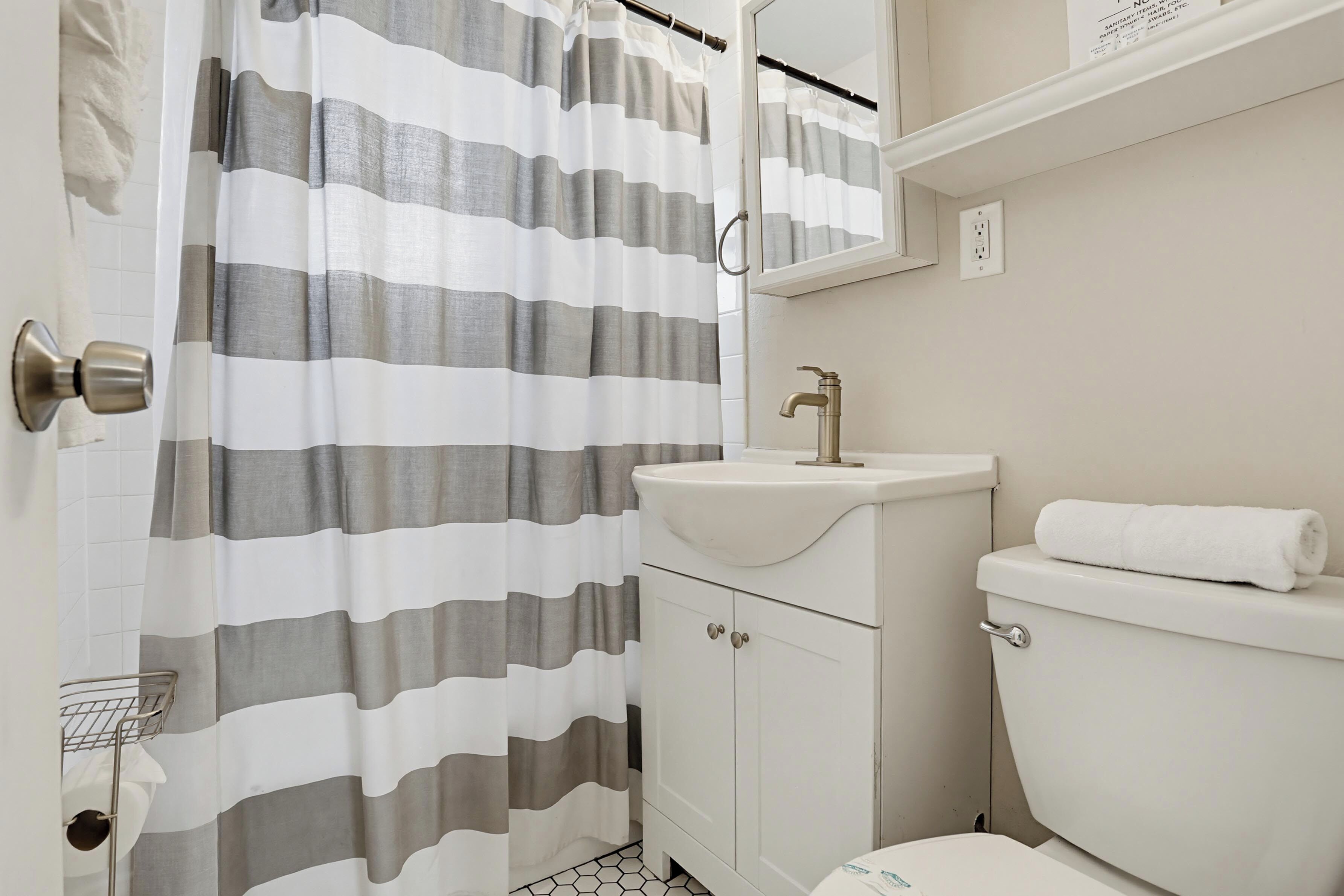Un baño con cortina de ducha a rayas, un lavabo, un inodoro y un espejo.