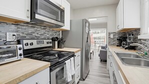 Een moderne keuken met een fornuis, magnetron en koelkast. Er is een raam boven het fornuis en een deur naar een andere kamer.