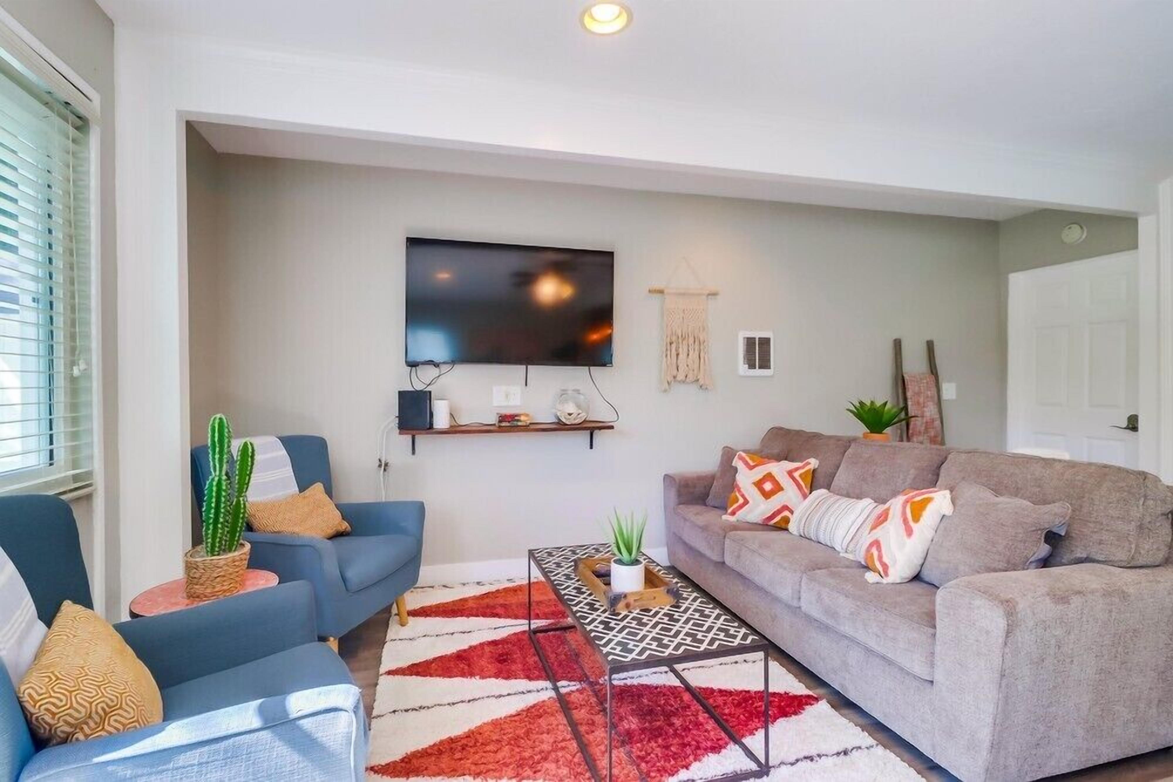 A living room with a grey sofa, a blue armchair, a coffee table, and a flat-screen TV mounted on the wall.