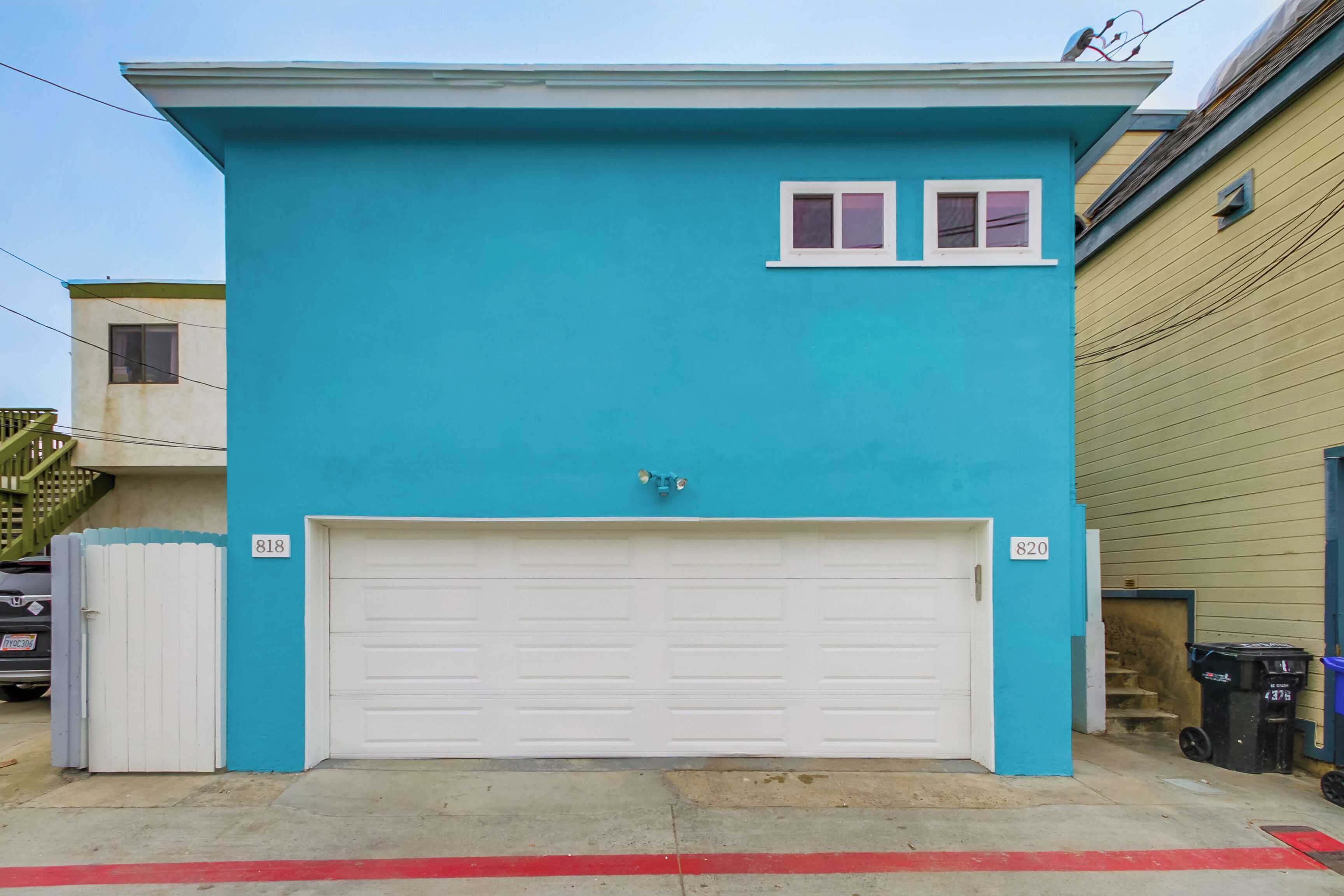 Een gebouw met twee verdiepingen, met een turquoise gevel, een witte garagepoort en twee ramen op de bovenverdieping.