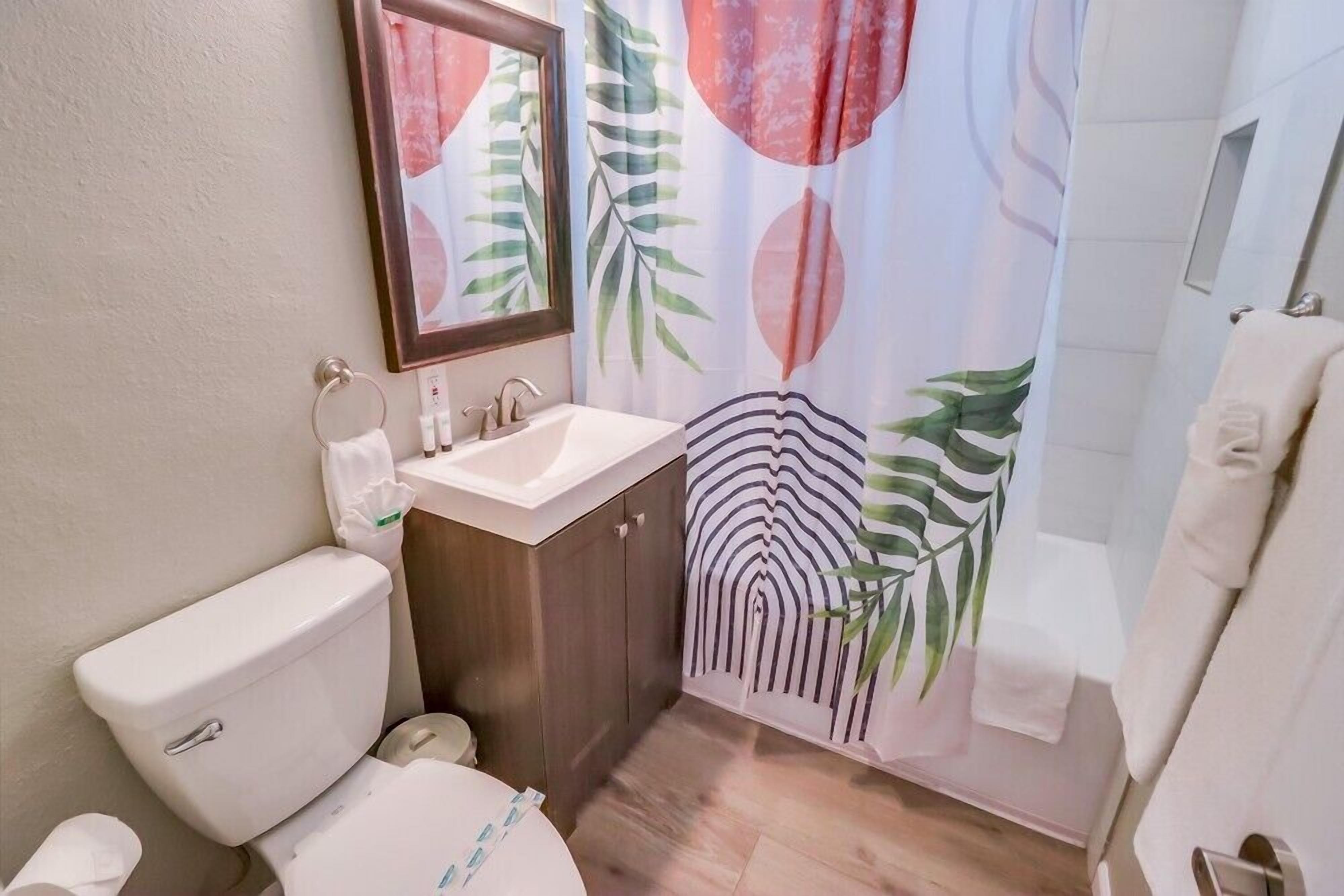 Un bagno con WC, lavandino e tenda della doccia con motivo a foglia tropicale.