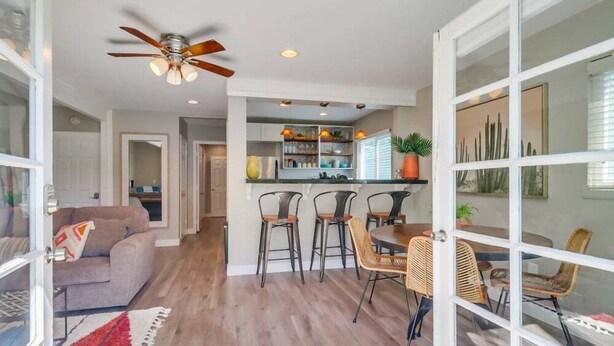 A spacious living area with a sofa, dining table, and chairs, a kitchen with bar stools, and a ceiling fan. - Casa Azul Lower (San Diego)