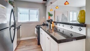 A modern kitchen with a black countertop, white cabinets, and a window with blinds. - Casa Azul Lower (San Diego)