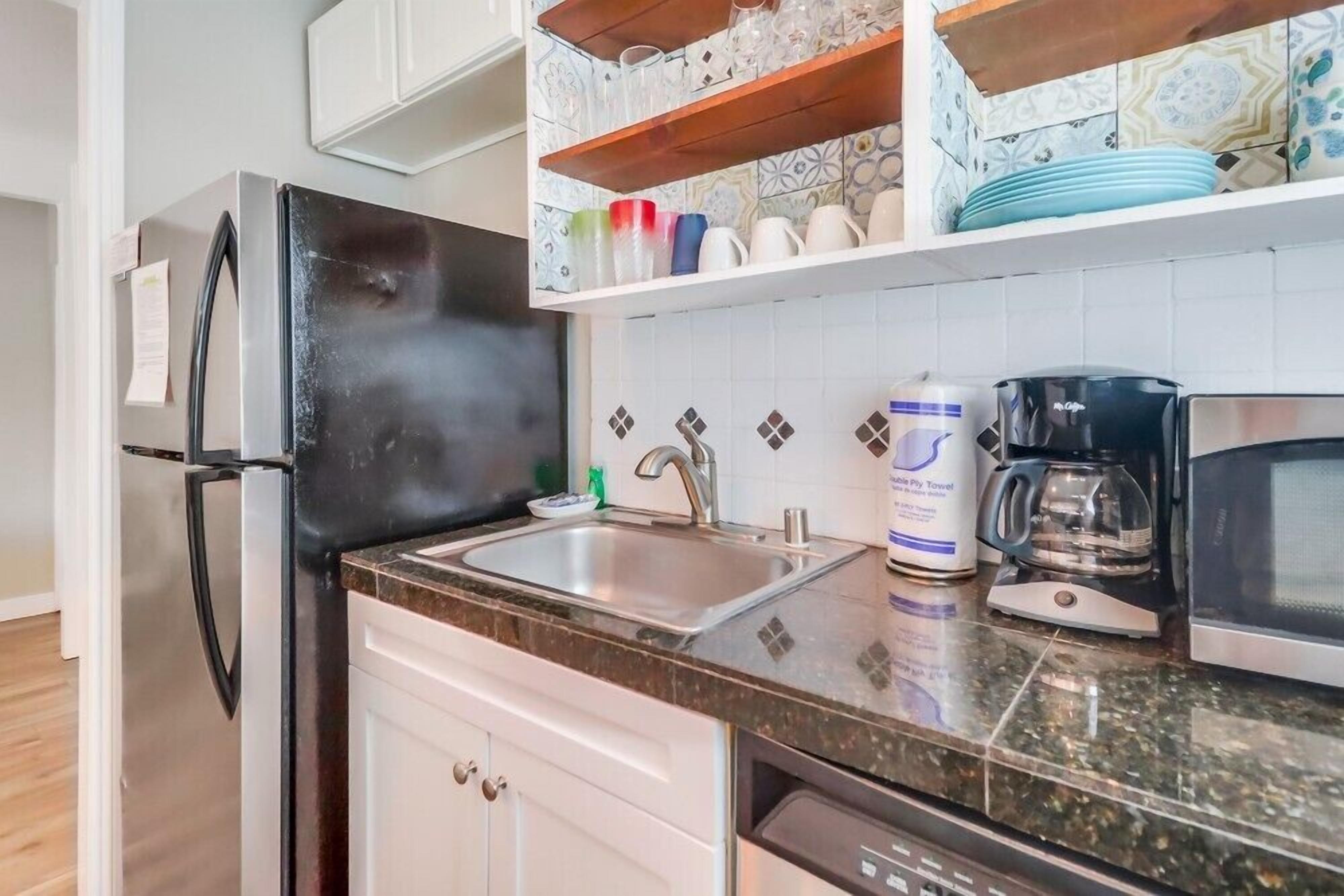 A kitchen with a stainless steel refrigerator, a sink, a coffee maker, and a microwave.