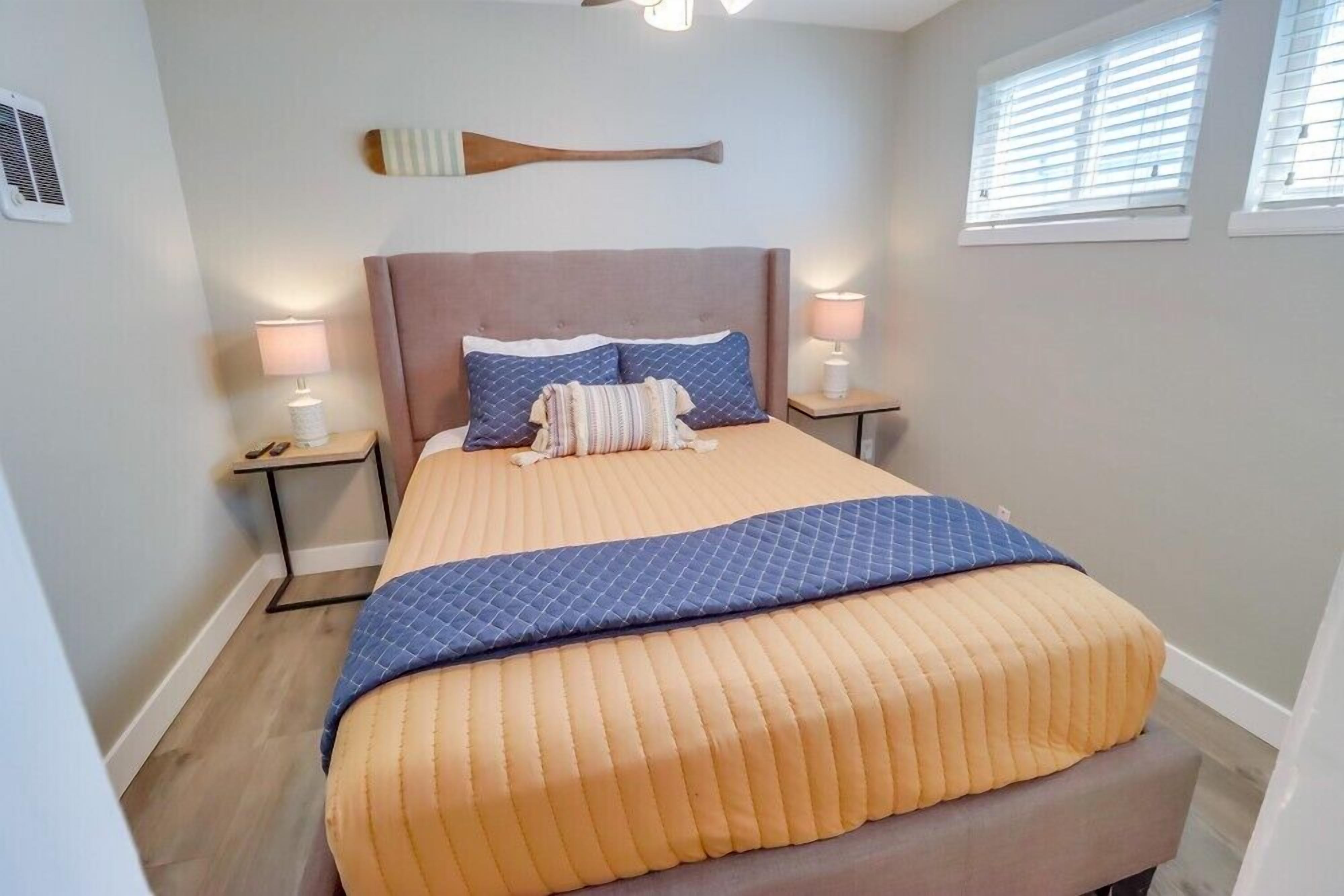 Una cama bien hecha con cabecera, dos lámparas de noche y una tabla de remo fijada a la pared.