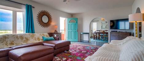 A living room with a sofa, a patterned rug, a ceiling fan, and a television.
