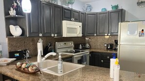 A kitchen with dark cabinets, a white microwave, a sink with a soap dispenser, and a refrigerator. - Southern Comfort at the Sonoran Sun (Puerto Peñasco)