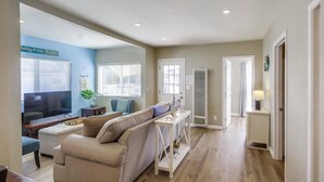 Un salon avec un canapé beige, un téléviseur et une petite table ornée d’objets décoratifs.
