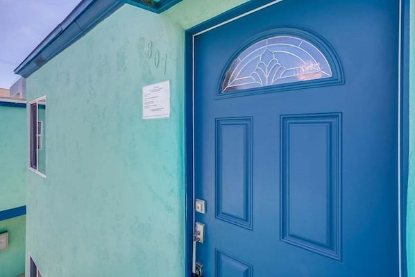 Un edificio azul verdoso con una puerta azul y un ventanal decorativo.