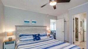 Ein Schlafzimmer mit einem Bett, Nachttischen, einem Deckenventilator und einer Tür zu einem Badezimmer.