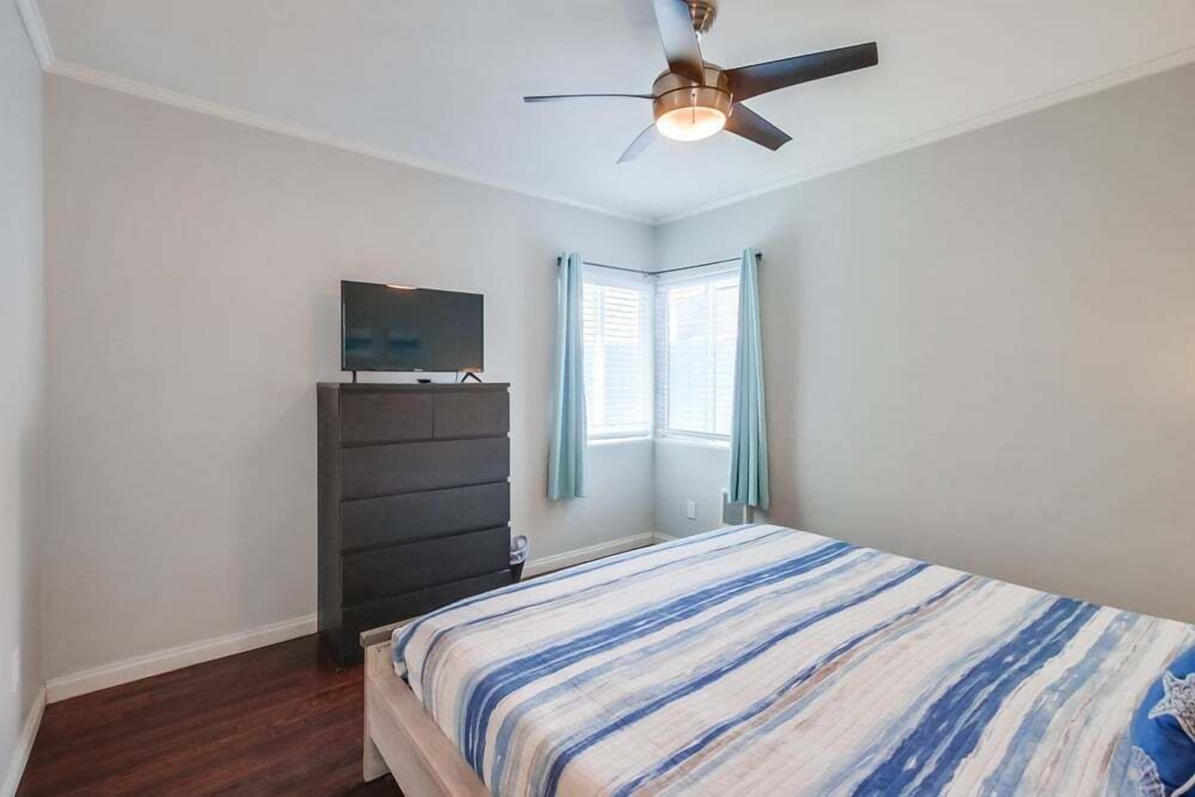 A bedroom with a bed, a dresser, a ceiling fan, and a window with curtains.