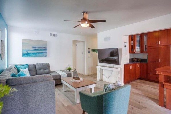 A living room with a sofa, a coffee table, a TV, and wooden cabinets. - Manhattan Shores 2 (San Diego)