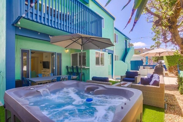 A backyard with a hot tub, outdoor furniture, and a building with a blue exterior. - Manhattan Shores 2 (San Diego)