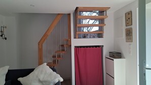 Un dormitorio con escalera de madera, cama con colcha blanca, cortina roja y decoración en la pared.
