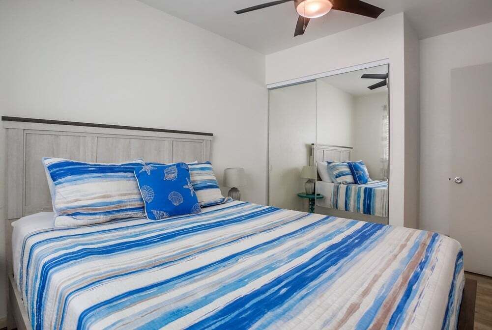 A bedroom with a bed, a ceiling fan, a nightstand, and a mirror.