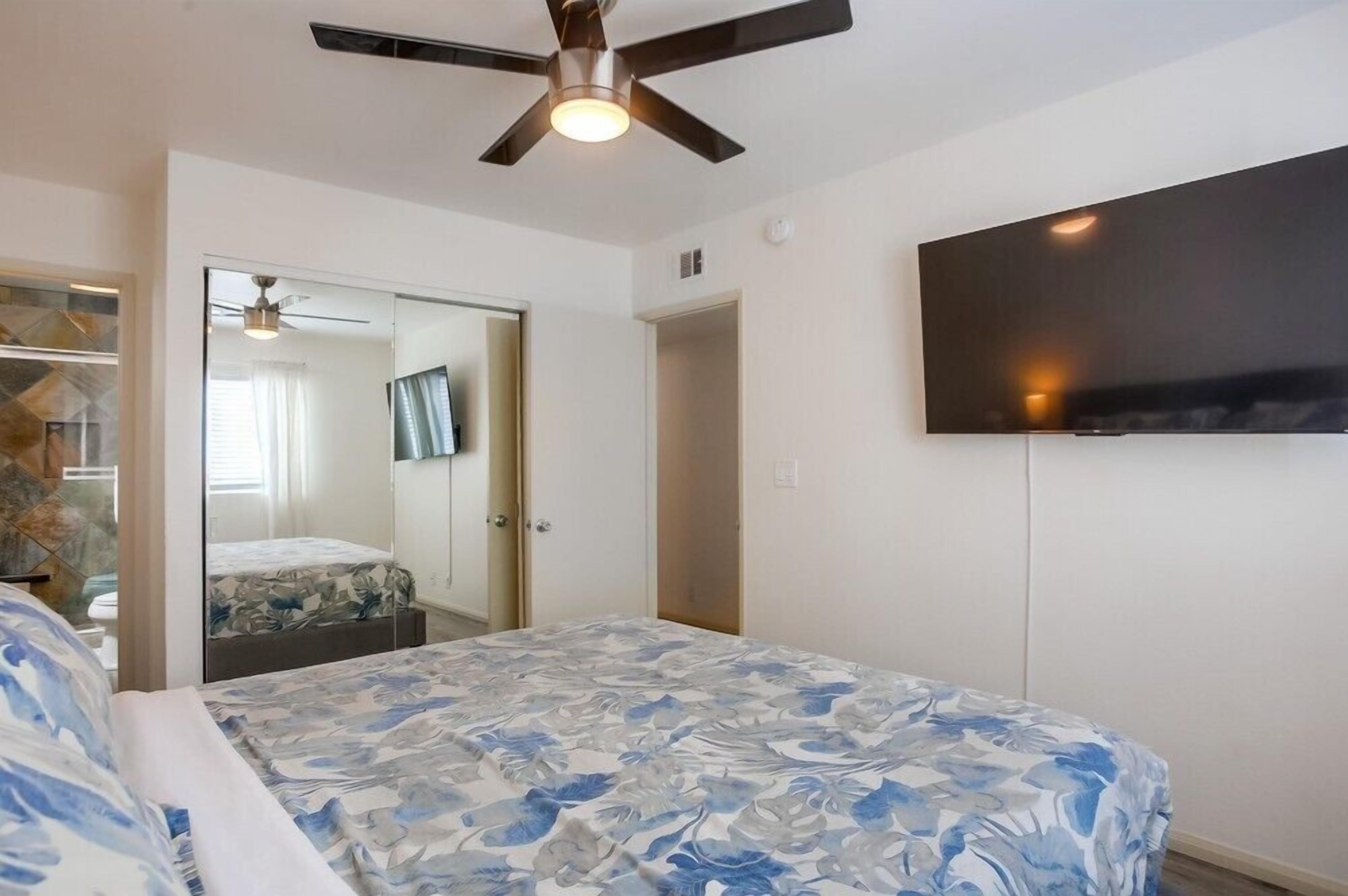 A bedroom with a bed, a ceiling fan, a TV, and a wardrobe.
