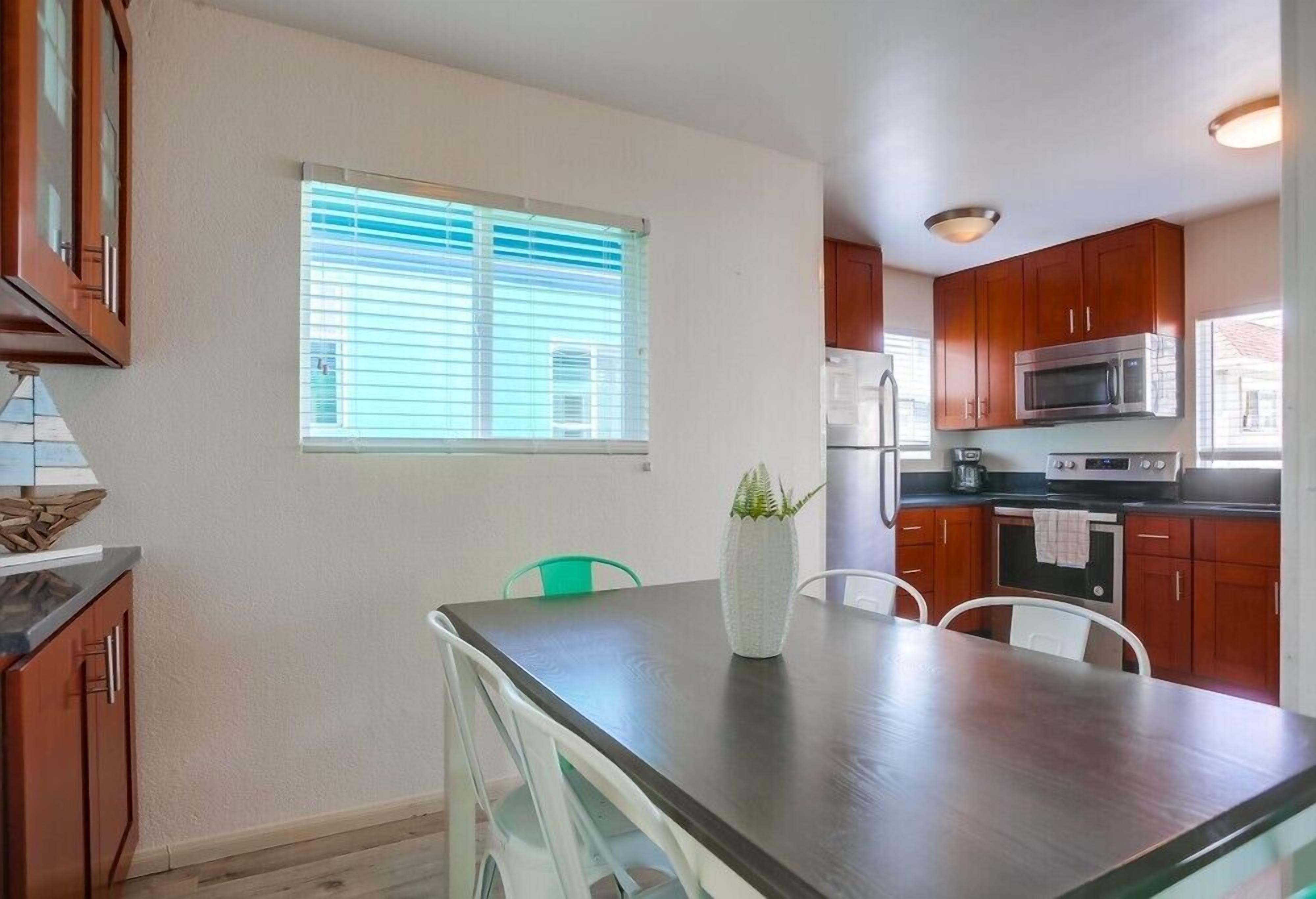 A modern kitchen with wooden cabinets, a stainless steel refrigerator, a microwave, and a dining area with a glass table and chairs.