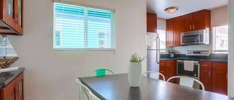 A modern kitchen with wooden cabinets, a stainless steel refrigerator, a microwave, and a dining area with a glass table and chairs.