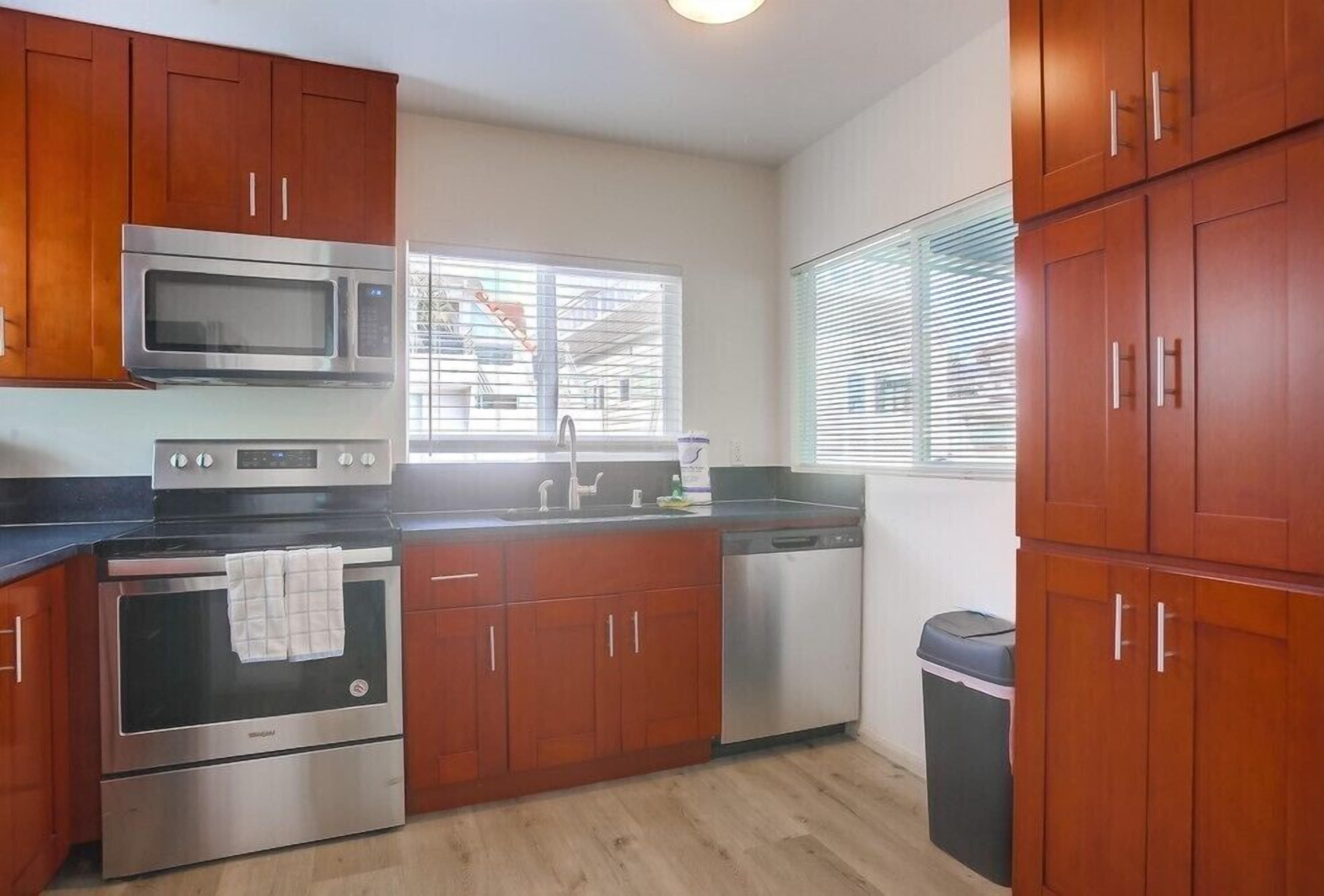 Una cocina con armarios de madera, electrodomésticos de acero inoxidable, una ventana y un cesto de basura.
