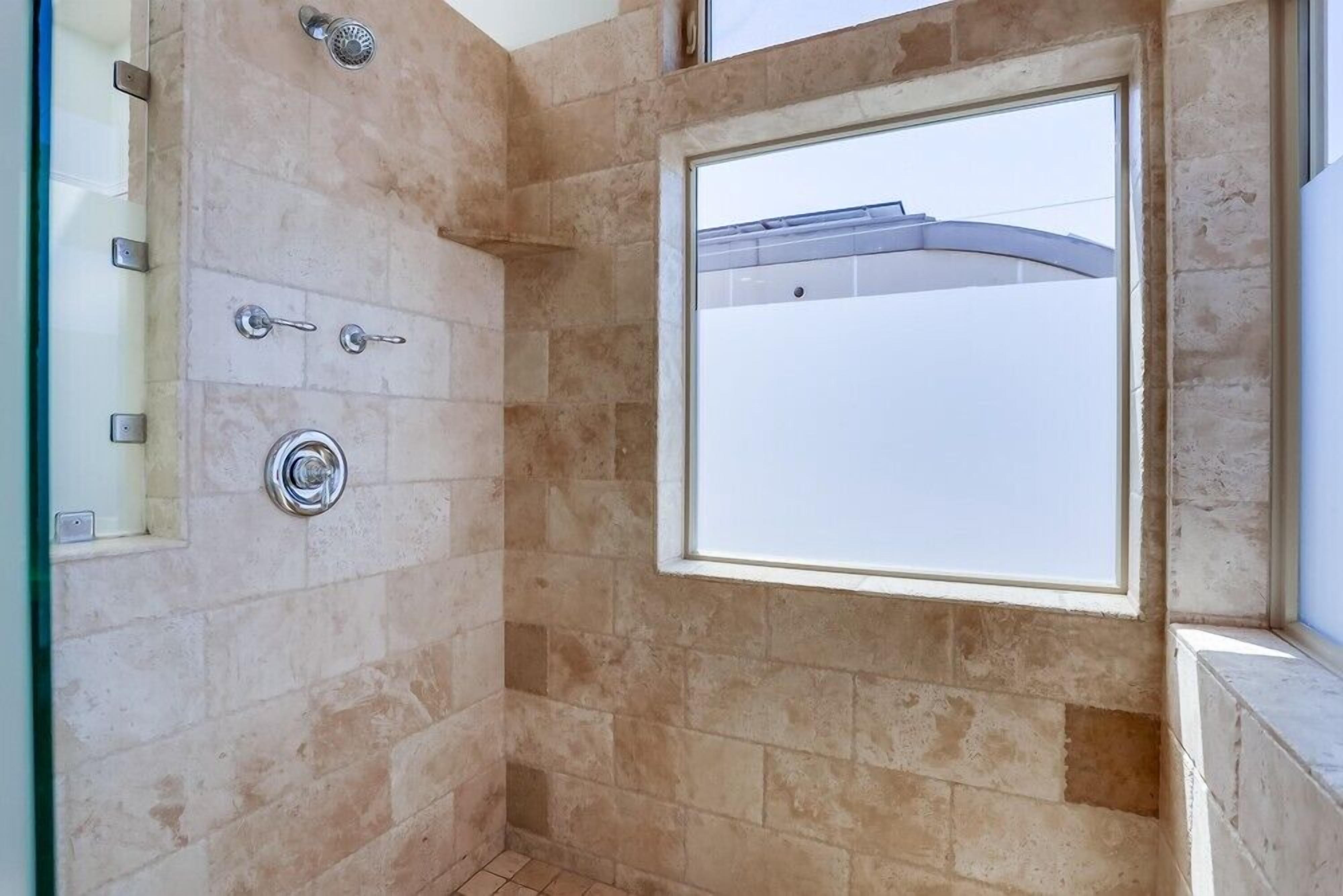 Ducha con puerta de vidrio, ventana y pared con azulejos.